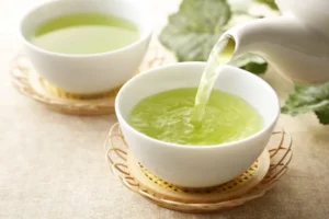 Cup of green tea with fresh leaves and lemon slices, rich in antioxidants like EGCG to support liver detox and health.